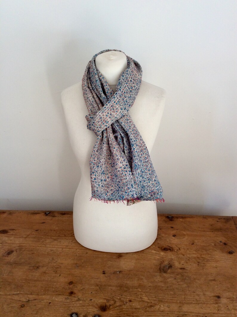 May include: A light blue and pink patterned scarf with a white background. The scarf is tied around a white mannequin.