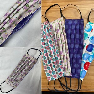 May include: Four fabric face masks with different patterns. One mask has a floral pattern, another has a polka dot pattern, another has a floral pattern with pink and blue flowers, and the last one has a blue and white pattern with circles. The masks are all pleated and have black elastic ear loops.