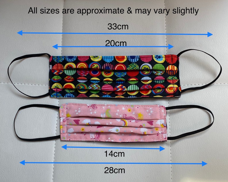 May include: Two face masks with black elastic ear loops. The top mask has a black background with colorful polka dots and measures 33 cm wide and 20 cm tall. The bottom mask has a pink background with a unicorn and rainbow pattern and measures 28 cm wide and 14 cm tall.