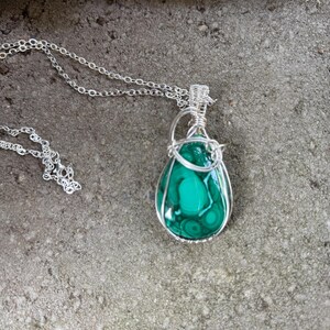 May include: A green malachite stone pendant wrapped in silver wire, hanging from a silver chain.