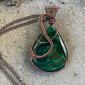 May include: A copper wire wrapped pendant featuring a green malachite stone. The pendant is attached to a copper chain.