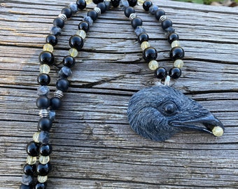 Raven Catches the Sun" pendant, hand carved and painted, hung from a strand of onyx, citrine and larvikite beads with silver accents.