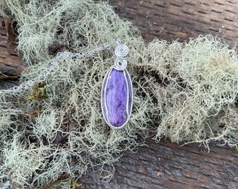 May include: A silver wire wrapped pendant featuring a purple and white chalcedony stone. The pendant is hanging from a silver chain.