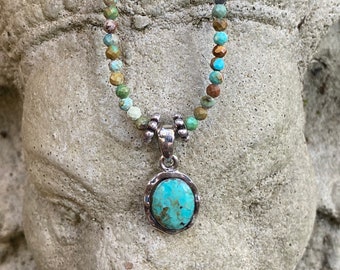 Turquoise pendant hung from a strand of tiny faceted turquoise beads with silver tone accents.