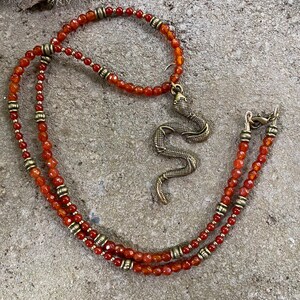 Brass snake pendant hung from strand of small faceted orange agate and tiny round carnelian beads with brass accents.