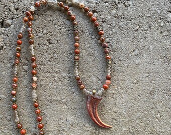 Velociraptor claw, actual size, replica hung from a strand of jasper and smoky quartz beads with brass accents.