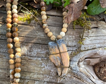 Replica Chilantaisaurus claw wire wrapped and hung from a strand of picture jasper and petrified wood beads with brass accents.