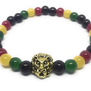 Puede incluir: Un brazalete con cuentas negras, rojas, amarillas y verdes. Un dije de cabeza de león dorado se encuentra en el centro del brazalete.