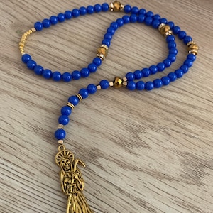 May include: A blue and gold rosary with a gold pendant featuring a skeletal figure holding a scythe.