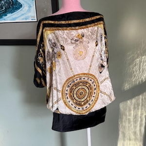 May include: A cream-colored silk top with a black border and a black bottom. The top features a gold and black ornate design with Roman numerals and chain details. The top is displayed on a pink mannequin.