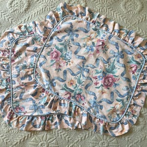 May include: Two pillowcases with a floral and ribbon pattern. The pillowcases have a light peach background with blue ribbons and floral bouquets in pink, blue, and yellow. The edges are ruffled and trimmed with a blue piping.