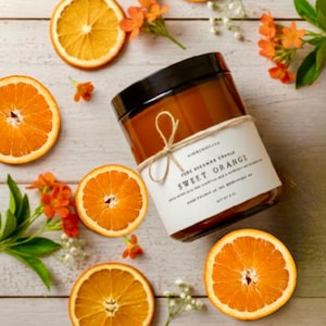 May include: A cylindrical amber glass candle jar with a black lid, wrapped in a white paper label tied with twine. The label reads Sweet Orange, Pure Beeswax Candle, and Net Wt 8 oz. The candle is surrounded by several bright orange slices.