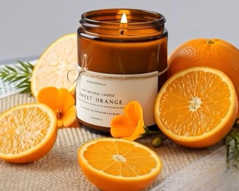 May include: A lit candle in a brown glass jar with a white label reading Sweet Orange, surrounded by several halved and whole oranges and small orange flowers. The candle features a visible flame and is tied with a thin piece of twine.