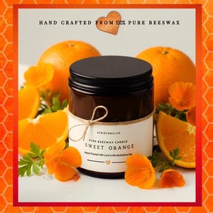 May include: A dark amber glass jar candle with a black lid and a white label reading ATBIRCHWILLCO PURE BEESWAX CANDLE SWEET ORANGE. The label is tied with twine and surrounded by fresh orange slices and bright orange flowers on a white surface.