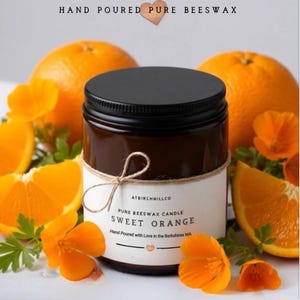 May include: A dark amber glass jar candle with a black lid and a white label reading HAND POURED PURE BEESWAX, ATBIRCHWILLCO, PURE BEESWAX CANDLE, SWEET ORANGE, Hand Poured with Love in the Berkshires MA, tied with a thin twine bow.