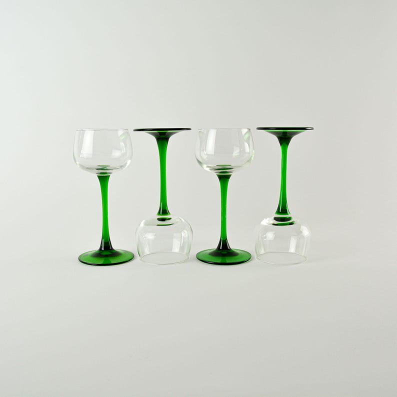 May include: Four clear wine glasses with green stems. Two glasses are upright, and two are inverted. The glasses have a classic design, with a rounded bowl and a slender stem. The green color adds a pop of color to the clear glass.