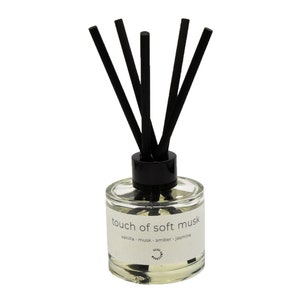 May include: A clear glass bottle diffuser with black reeds and a white label that reads "touch of soft musk" and "vanilla - musk - amber - jasmine".