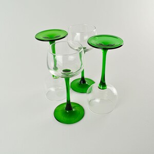 May include: Four clear wine glasses with green stems and bases. Two glasses are upright, while the other two are inverted. The green stems and bases provide a striking contrast against the clear glass bowls.