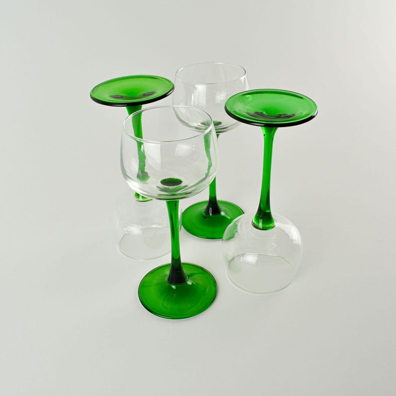 May include: Four clear wine glasses with green stems and bases. Two glasses are upright, while the other two are inverted. The green stems and bases provide a striking contrast against the clear glass bowls.