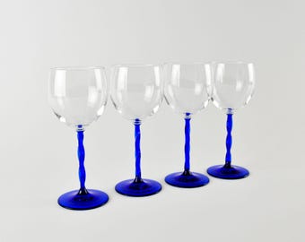 May include: Four clear wine glasses with cobalt blue twisted stems and bases. The glasses are arranged in a row against a white background. The stems have a unique, decorative design, adding a touch of elegance to the glassware.