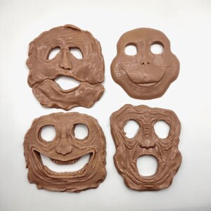 May include: Four light brown, textured face masks with distinct facial expressions. Each mask features cutouts for eyes and a mouth, showcasing varied, irregular shapes and detailed, wrinkled surfaces that create unique, expressive character designs.