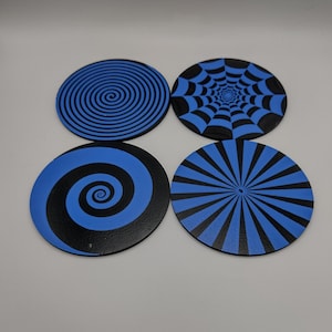 May include: Four round coasters with black and blue designs. The designs include a spiral, a spider web, a swirl, and a sunburst pattern. These coasters are a decorative and functional addition to any home.