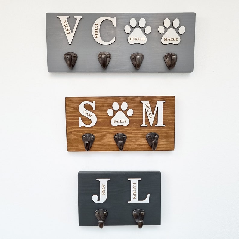 May include: Three wooden wall-mounted coat racks in gray, brown, and dark gray. Each rack has metal hooks and personalized white lettering. The top rack has the names Vicky, Chris, Dexter, and Maisie. The middle rack has Sam, Bailey, and Megan. The bottom rack has Josh and Lauren.
