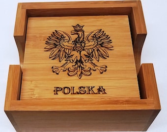 Op de afbeelding: Een set van vier vierkante bamboe onderzetters met een houder. Elke onderzetter heeft een gedetailleerde gravure van het Poolse wapen, een gekroonde adelaar, en het woord "POLSKA" eronder. De onderzetters en de houder zijn gemaakt van lichtbruin bamboe.