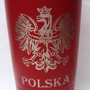 May include: A red insulated tumbler with a silver rim and lid. The Polish coat of arms, an eagle with a crown, is etched in silver, along with the word "POLSKA".