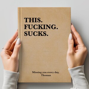May include: A brown notebook with the text "THIS. FUCKING. SUCKS." and the message "Missing you every day, Thomas" on the front cover.