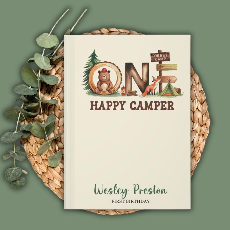 Puede incluir: Un libro de color crema con un tema de bosque. La portada presenta la palabra "ONE" en letras marrones con ilustraciones de un oso, un zorro y una tienda de campa&ntilde;a. El texto "Happy Camper" est&aacute; debajo de la palabra "ONE". La parte inferior de la portada dice "Wesley Preston Primer Cumplea&ntilde;os".