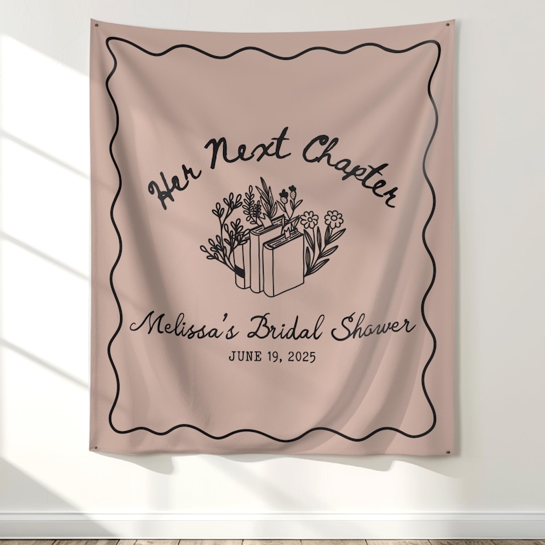 Op de afbeelding: Een blush-kleurige stoffen banner met zwarte tekst en een decoratieve rand. De banner leest "Her Next Chapter" boven "Melissa's Bridal Shower" en de datum "June 19, 2025". Een bloemen- en boekillustratie is gecentreerd.