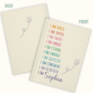 Pu&ograve; includere: Quaderno color crema con il testo "I AM LOVED, I AM JOYFUL, I AM SMART, I AM UNIQUE, I AM STRONG, I AM ENOUGH, I AM GRATEFUL, I AM CONFIDENT, I AM BEAUTIFUL, I AM Sophia" in colori arcobaleno. Un disegno di farfalla e cuore &egrave; presente sul fronte e sul retro.