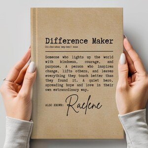 May include: A brown notebook with the text "Difference Maker" and a definition of the word. The notebook also includes the text "ALSO KNOWN: Raefene".