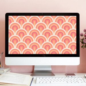 May include: A white desktop computer with a modern design. The screen displays a retro-style pattern of overlapping orange, pink, and white arches. The computer is sitting on a white desk with a keyboard and a cell phone.