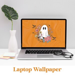 May include: A laptop computer with a Halloween-themed wallpaper featuring a white ghost with a floral wreath around it on an orange background. The text "Laptop Wallpaper" is displayed below the laptop.