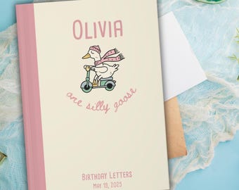 May include: A personalized notebook with a light beige cover and pink spine. The cover features the name "OLIVIA" in pink, along with a cartoon goose riding a scooter and the phrase "are silly goose". The bottom reads "BIRTHDAY LETTERS MAY 19, 2025".
