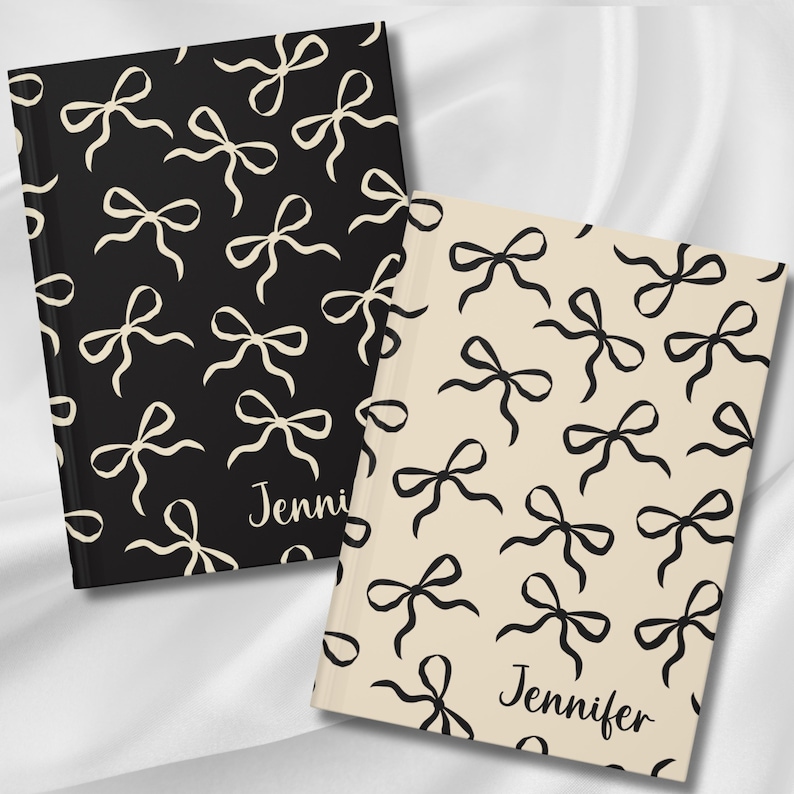 May include: Two personalized notebooks with a black and white bow pattern. The notebook on the left has a black cover with cream bows and the text "Jenni" on the bottom. The notebook on the right has a cream cover with black bows and the text "Jennifer" on the bottom.