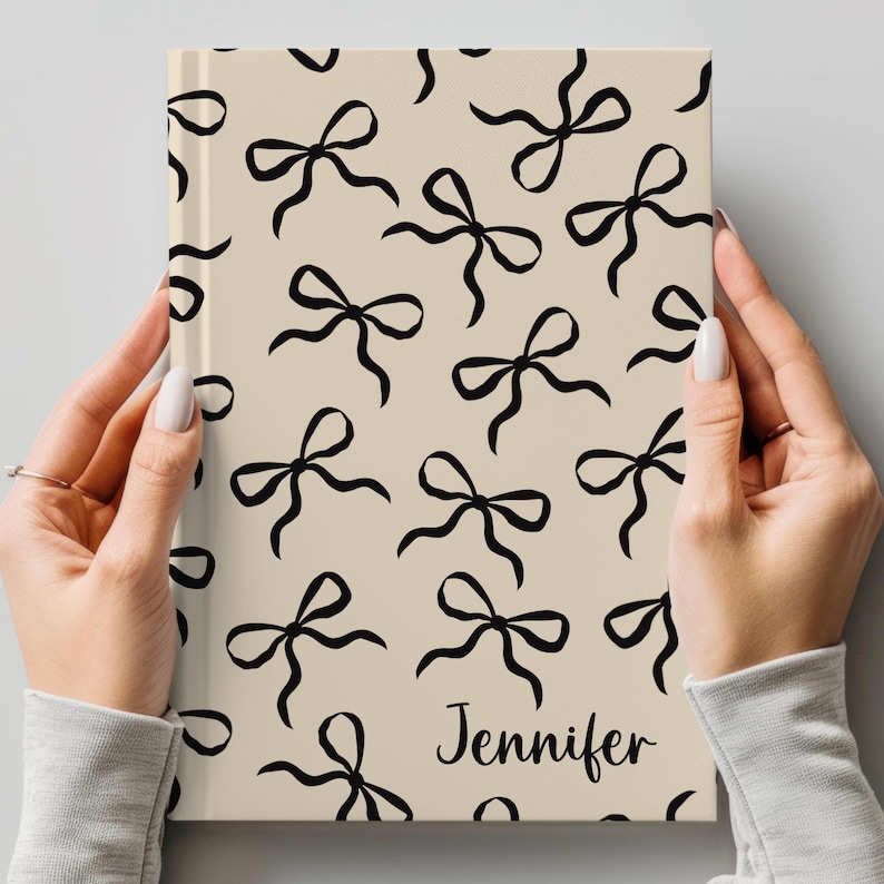 May include: A beige notebook with a black and white bow pattern and the name "Jennifer" printed on the cover.