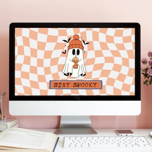May include: A computer monitor displays a Halloween-themed graphic. The design features a cartoon ghost wearing an orange beanie and holding a drink. The background is a wavy orange and white checkered pattern, with the text "STAY SPOOKY" at the bottom.