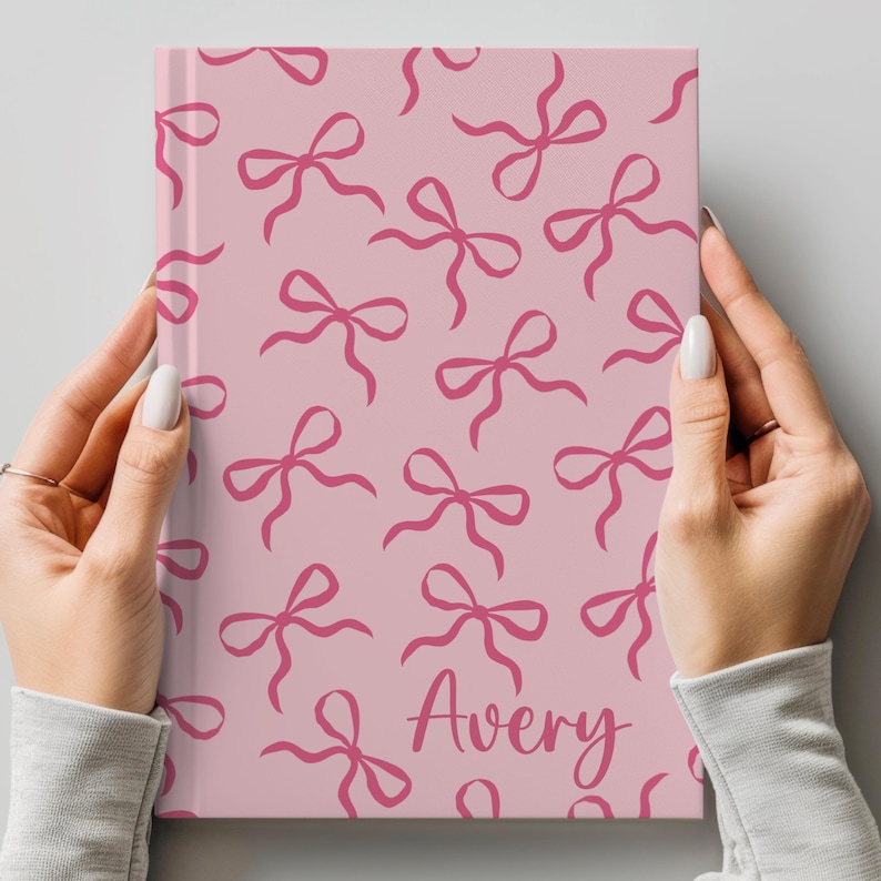 May include: A pink notebook with a pattern of pink bows and the name "Avery" written in pink cursive.