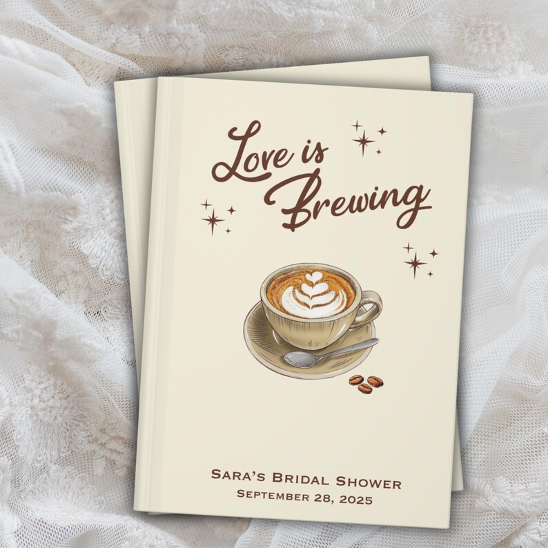 May include: Two stacked cream-colored books with the text "Love is Brewing" and a coffee cup illustration. The cup is on a saucer with a spoon and coffee beans. Below is "Sara's Bridal Shower, September 28, 2025."