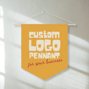 May include: A mustard yellow fabric wall pennant hanging from a wooden dowel with a white string. The pennant features the text "CUSTOM LOGO PENNANT" in large, bold, off-white letters, with the phrase "for your business" in red cursive script below.