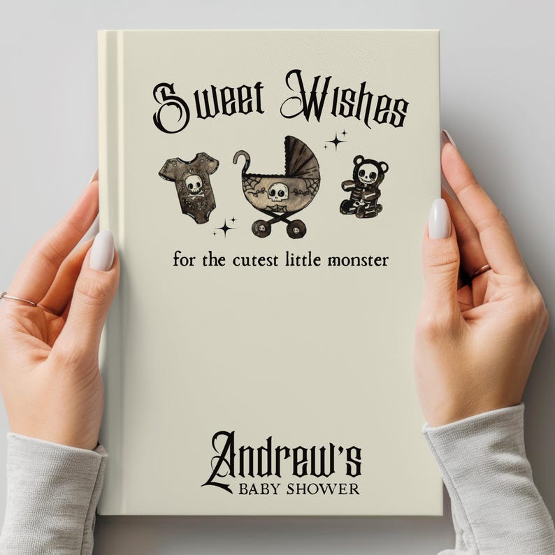 May include: A cream-colored baby shower guest book with the text "Sweet Wishes" and "for the cutest little monster." The book features illustrations of a onesie, stroller, and teddy bear, each with a skull design. The name "Andrew's" and "Baby Shower" are also printed on the book.