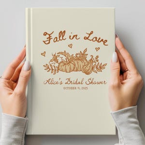 May include: Cream-colored journal with the text "Fall in Love" in brown script, along with a pumpkin and leaf illustration. The journal is personalized with "Alice's Bridal Shower" and the date October 11, 2025.