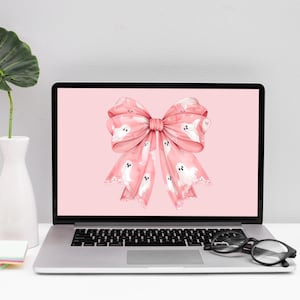 May include: A pink laptop computer with a pink bow with white ghost patterns on the screen. The bow is tied in a knot in the center. The laptop is on a white surface.