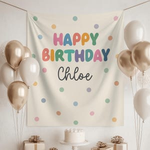 May include: A cream-colored fabric backdrop featuring the text "HAPPY BIRTHDAY Chloe" in colorful, rounded letters, surrounded by scattered polka dots in various pastel shades. The banner is framed by clusters of metallic gold and white balloons.