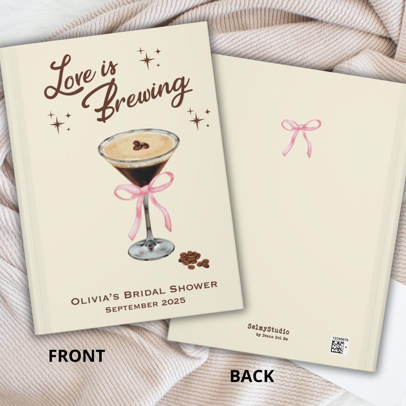May include: A cream-colored bridal shower guest book with the text "Love is Brewing" and a watercolor illustration of a coffee martini with a pink ribbon. The back of the book has a pink bow illustration.