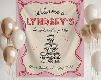 May include: A pink and cream bachelorette party banner with the text "Welcome to LYNDSEY'S bachelorette party" and a champagne glass pyramid. The banner also includes the location and date of the party, and is decorated with balloons.