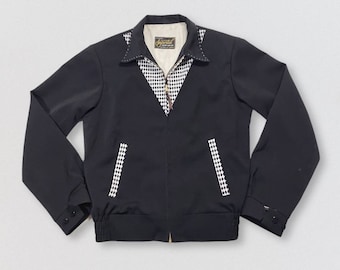 May include: A black zippered jacket with a checkered pattern on the collar and pockets. The jacket has a gold zipper and a label that reads "Jaymar" on the collar.